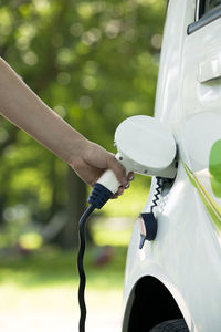 Cropped hand of woman charging electric car at station