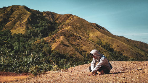 Young man sitting on field against mountain