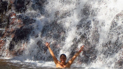 Portrait of happy woman with arms raised against waterfall