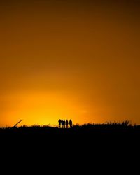 Silhouette of men on field against sky during sunset