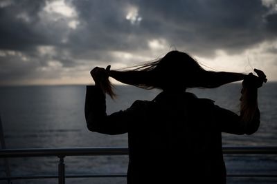 Rear view of silhouette woman standing by sea against sky