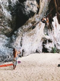 Man looking at woman climbing rock at beach