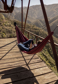 Man relaxing on hammock by mountain against sky