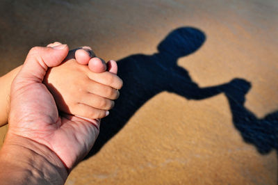 Cropped image of father holding baby hand at beach