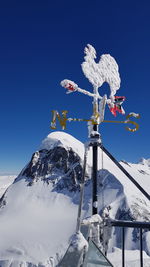 Low angle view of frozen weather vane against mountains and clear blue sky during winter