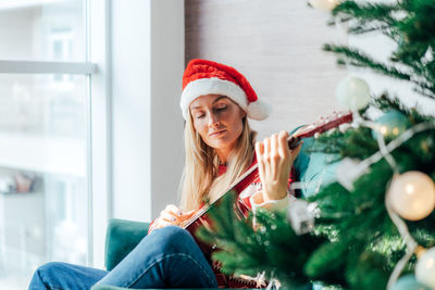 Smiling young woman sitting by christmas tree