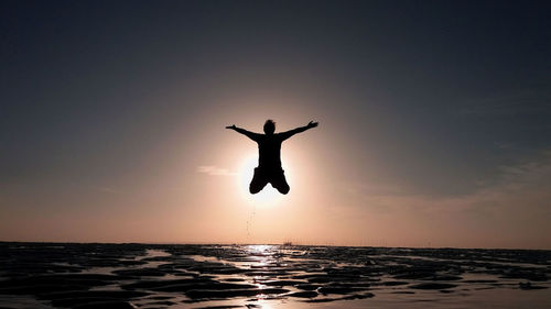 Silhouette man surfing in sea against sky during sunset