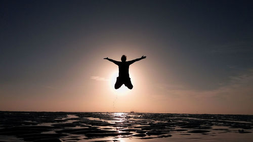 Silhouette man jumping over sea against sky during sunset