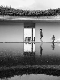 Father and son by building entrance reflecting in pond