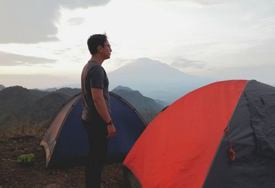 Man standing by tent on mountain against sky