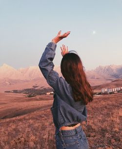 Rear view of woman with arms raised standing against landscape