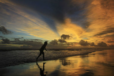 Silhouette man on beach against sky during sunset