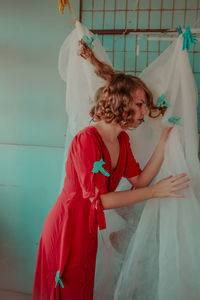 Thoughtful woman in red dress with curtain at home