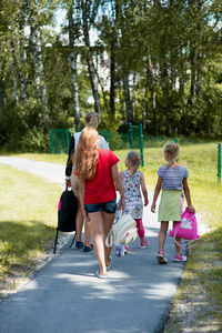 Rear view of girls walking on road along trees