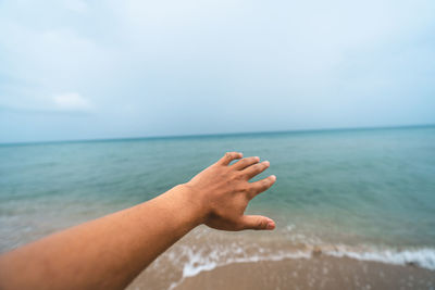 Midsection of person hand on sea against sky