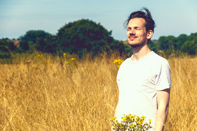 Smiling young man standing on land against sky