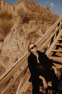 Woman wearing sunglasses while sitting on staircase against mountain