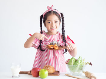 Portrait of smiling girl pointing at pretzel against white background