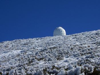 Low angle view of snowcapped mountain against clear blue sky
