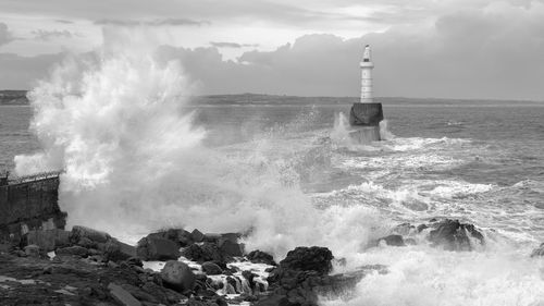 Waves splashing on rocks at shore against sky