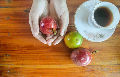 High angle view of hands holding passion fruits beside a cup of coffee on table