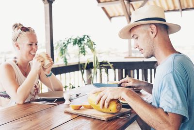 Man cutting fruit while sitting with female friend on table