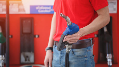 Man red uniform holding pump nozzle for service at gas station.