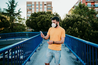 Young man using mobile phone while standing on railing