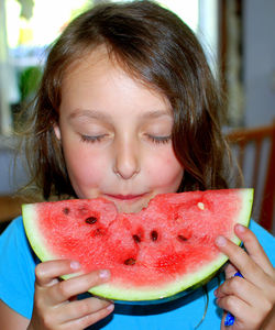 Girl with closed eyes eating watermelon at home