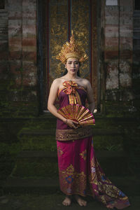 Portrait of young woman standing against built structure