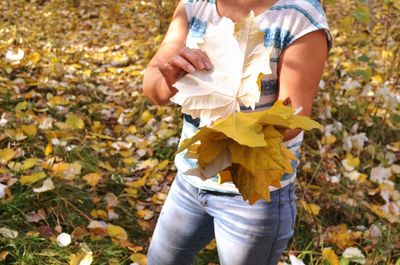 Midsection of woman collecting fallen dry leaves at public park during autumn