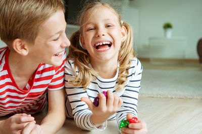 Portrait of cheerful siblings playing with dice while lying on carpet at home