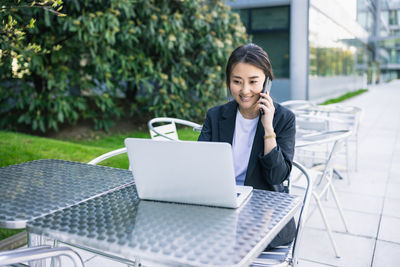 Asian business woman talking on phone and working with laptop outdoor