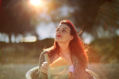 Redhead woman holding hat during sunset