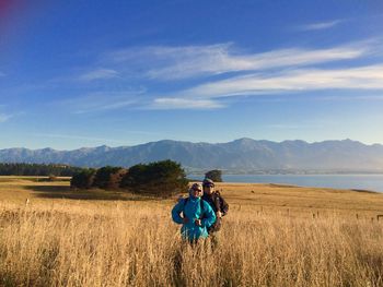 Couple standing on grassy field against blue sky