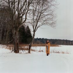 A woman stands on the shore of a frozen lake in a yellow scarf