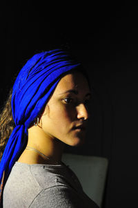 Close-up of woman wearing blue headwear against black background