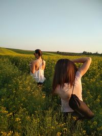 Friends standing amidst flowering plants on field against sky