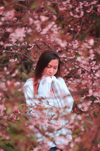 Woman standing by pink cherry blossom tree