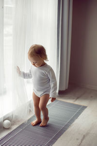 Girl child stands at the window in white clothes at home in winter