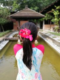 Rear view of woman standing by pond against built structure