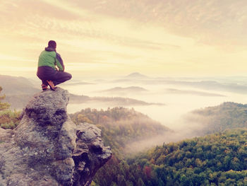 Man standing on rock looking at mountain against sky