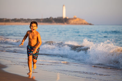 Little kid running on the beach with a lighthouse background