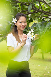 Portrait of smiling woman standing by flowering plants