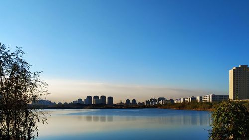 Lake and buildings against clear blue sky