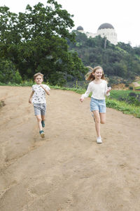 Full length of brother and sister running on dirt road