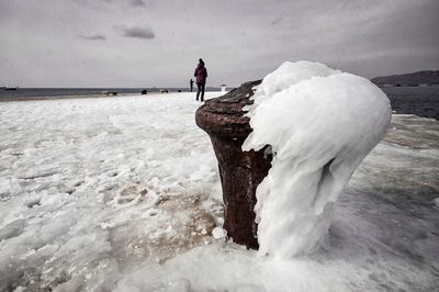 Man standing on snow covered shore against sky