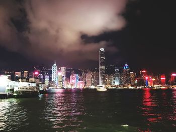 Illuminated buildings by river against sky at night