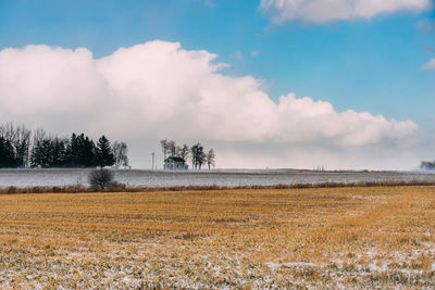 Farm house on the horizon. plowed field with a snow covered field beyond.