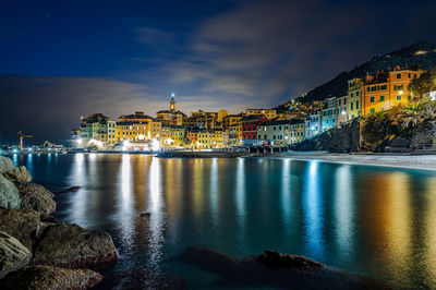 Illuminated buildings by river against sky at night